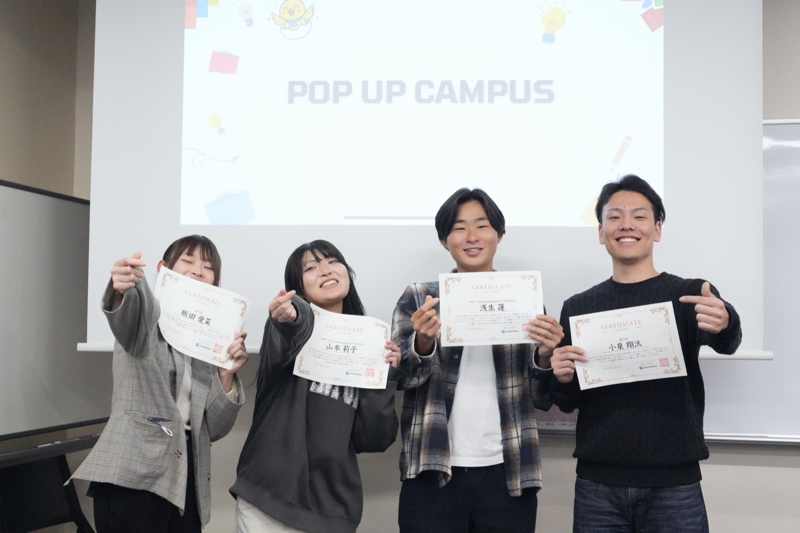 修了証を手にした学生たちがスクリーンの前で笑っている様子