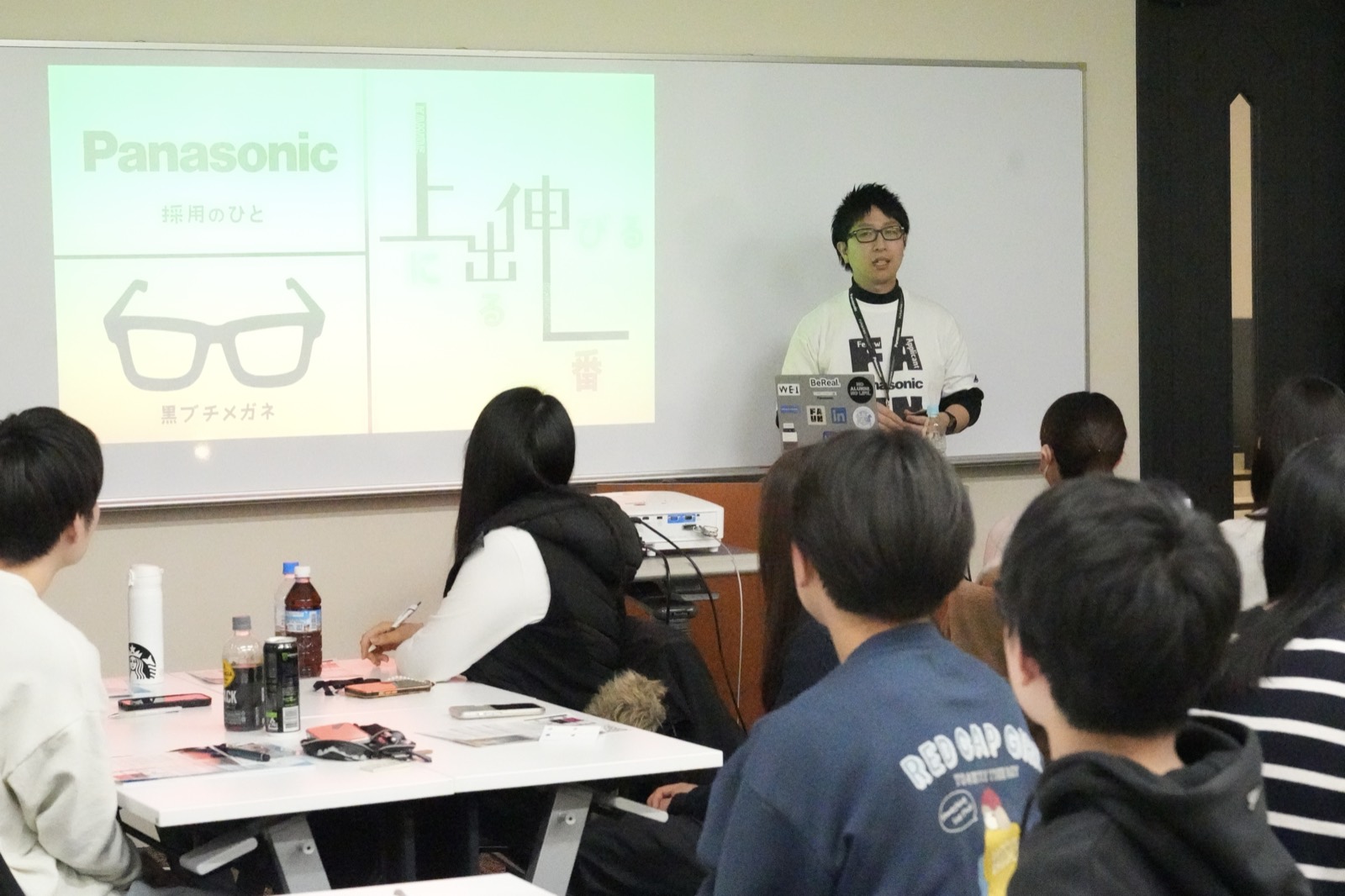 企業の社員がスライドを使って学生に仕事を紹介している様子